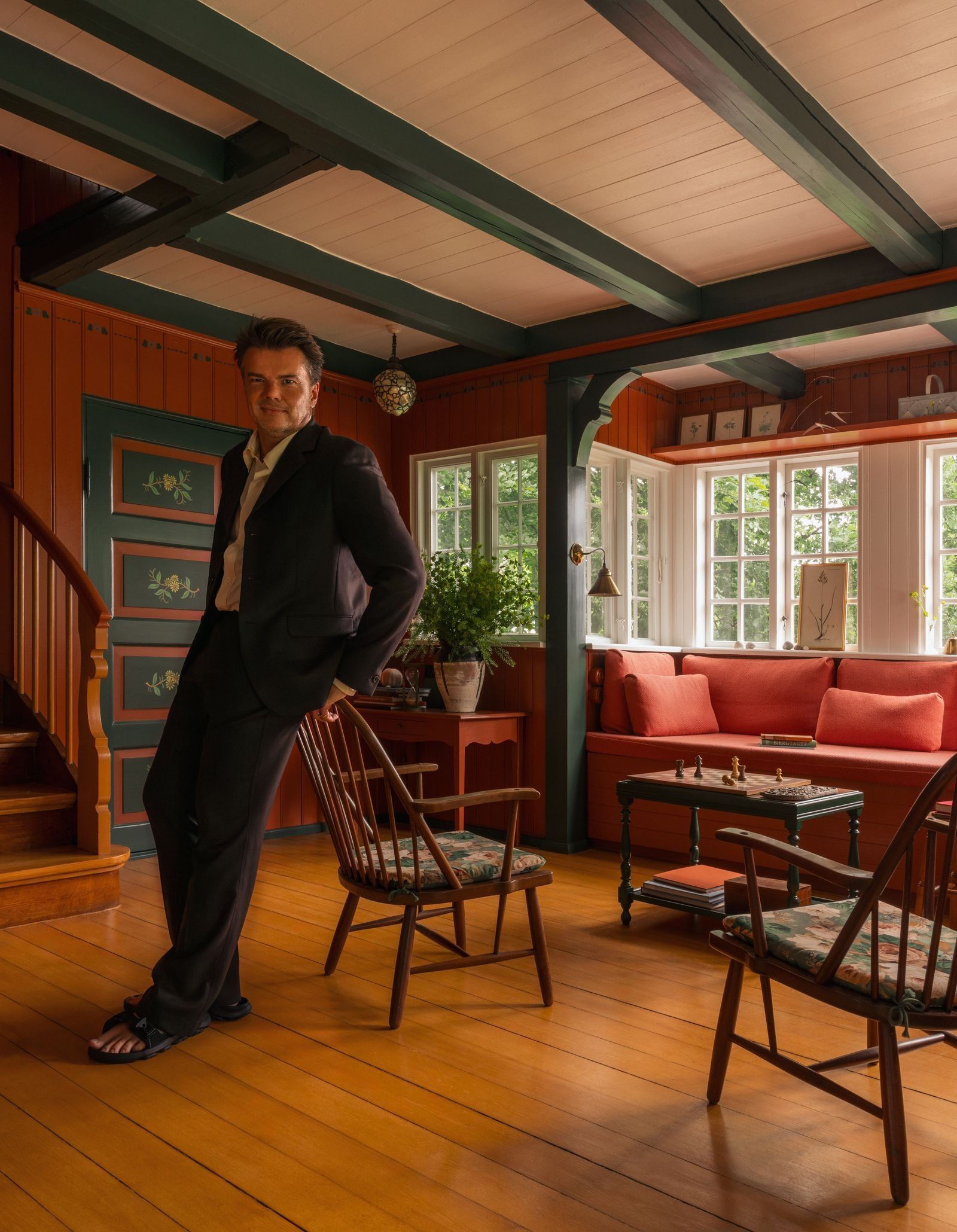 Bjarke Ingels en su casa de verano en un salón con sillas de madera paredes rojas y sof rojo.