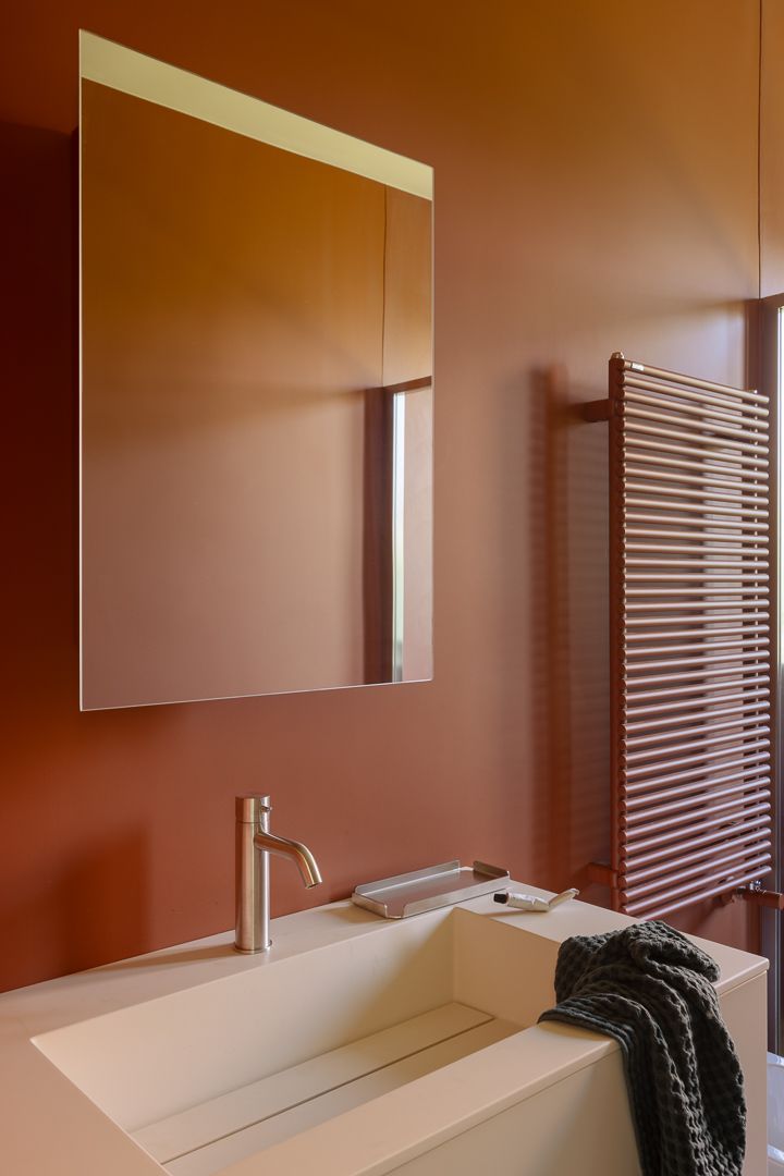 baño con espejo lavabo y paredes rojo ladrillo.