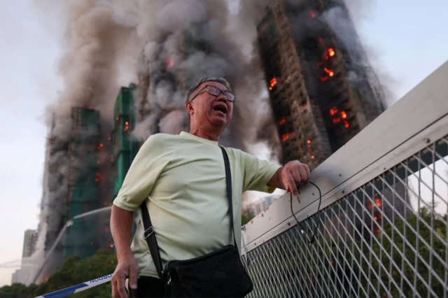 Un hombre llora mientras en el fondo se incendian edificios del complejo Wang Fuk Court en Hong Kong