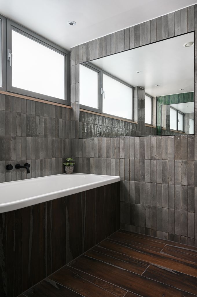 Cuarto de baño con espejo en pared de azulejos oscuros