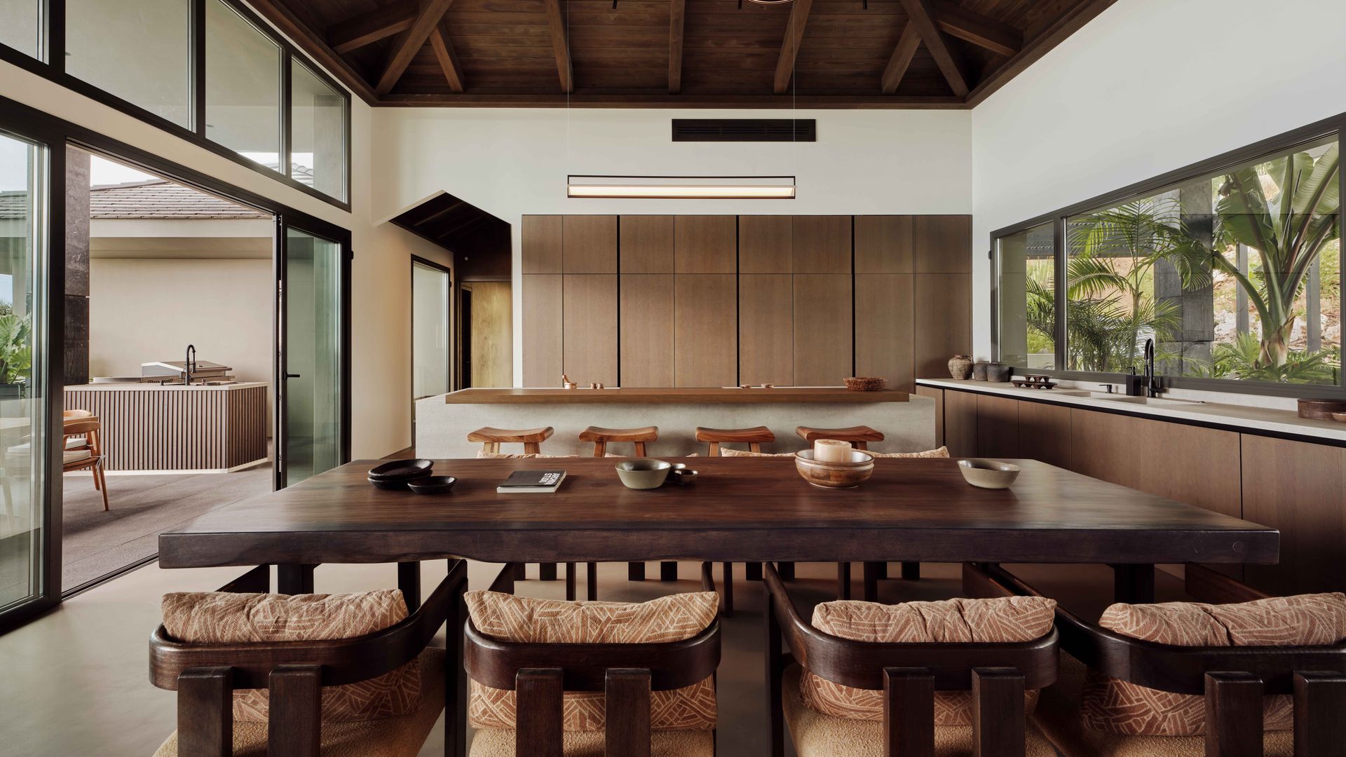 Cocina con comedor, techo de madera, mesa de madera, lámpara de techo. sillas de madera, muebles de cocina sin tiradores, ventanales que comunican jardín 