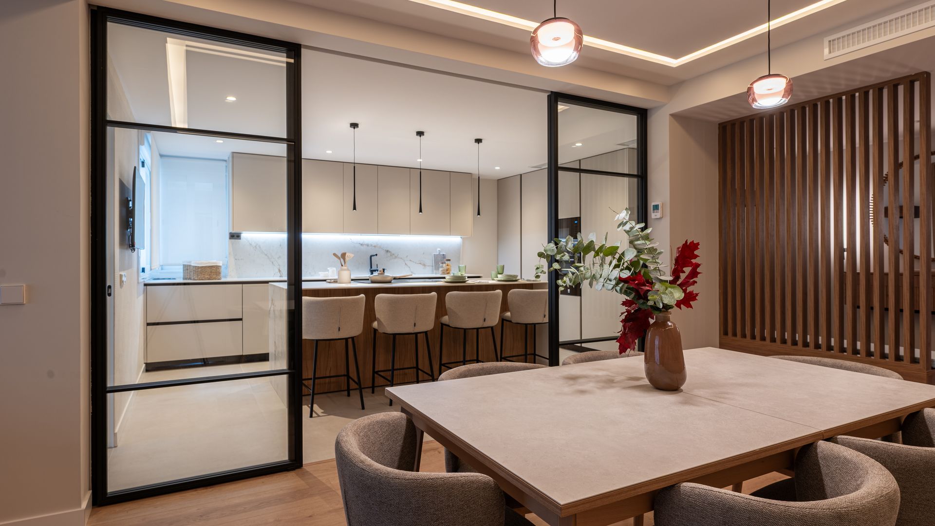 Cocina con comedor independizada con tabiques de cristal con los perfiles negros, lámparas de techo, mesa de comedor, sillas de comedor tapizadas