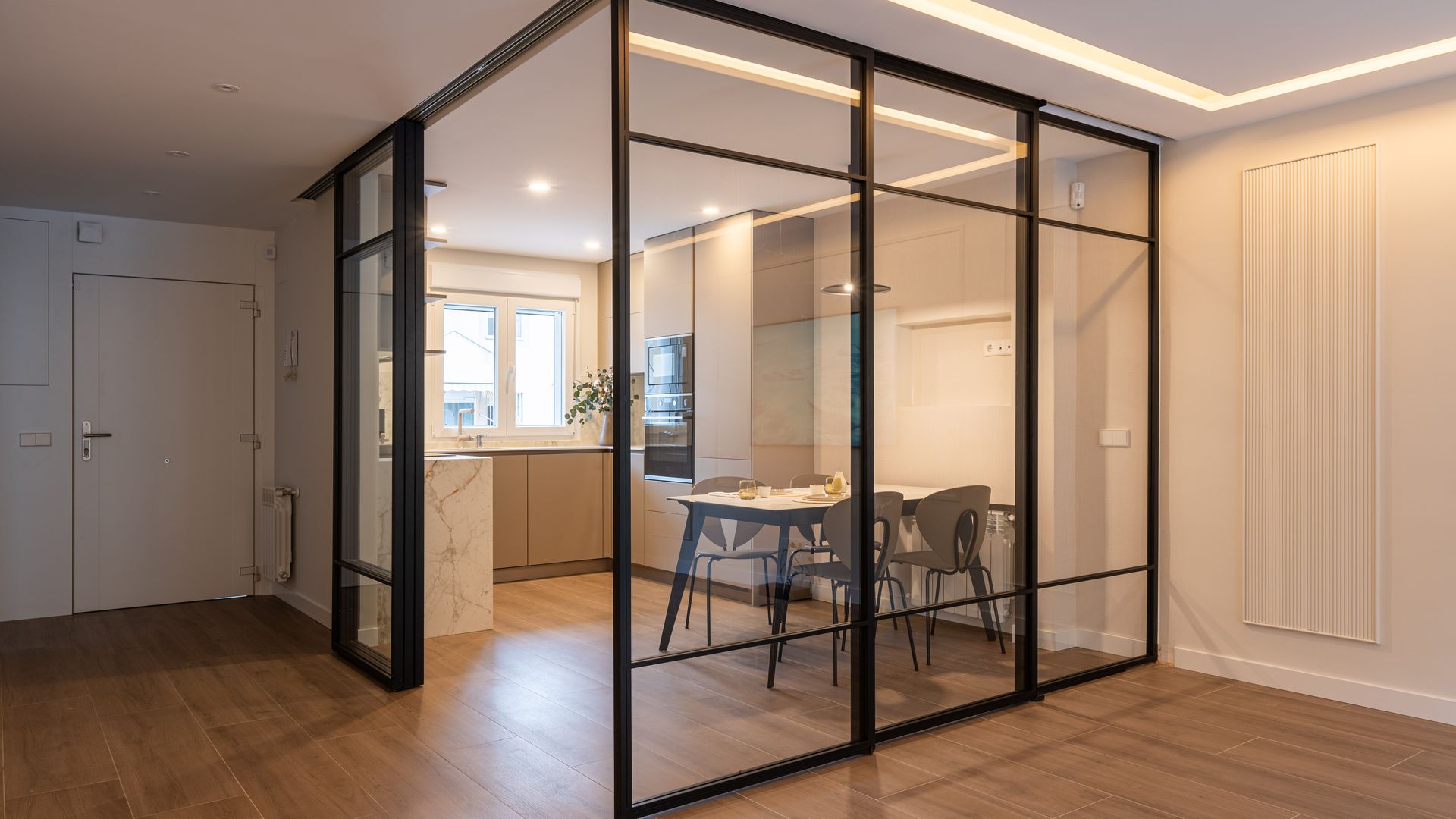 Cocina con comedor metida en una urna de cristal con perfiles negros y suelo de madera