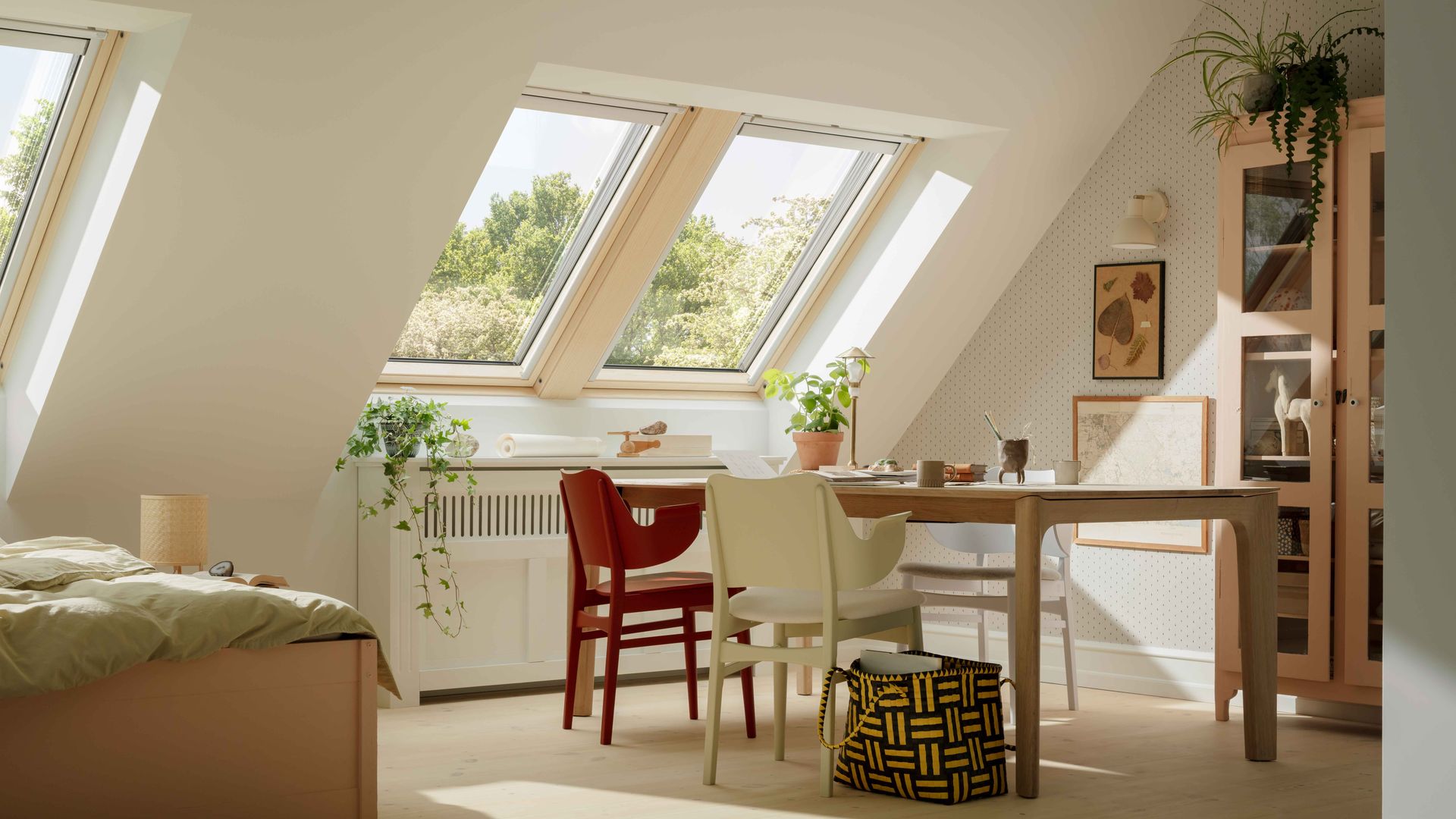 Piso pequeño con mesa de comedor, cama, ventanas de techo Velux, sillas de colores, vitrina de madera