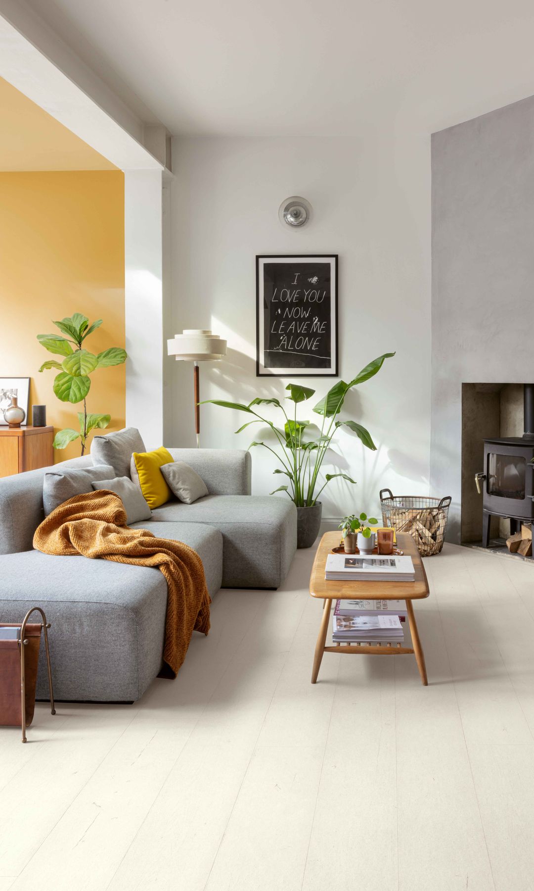 Salón con chimenea, sofá gris, mesa de centro de madera, suelo laminado, revistero, plantas, cuadro en la pared, manta en el sofá