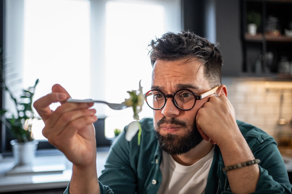 Sad young man disgusted by unhealthy food on fork in kitchen sad young man sitting in a modern kitchen, looking down with disgust at the unhealthy meal before him, reflecting disappointment over his dietary choices and unhealthy lifestyle