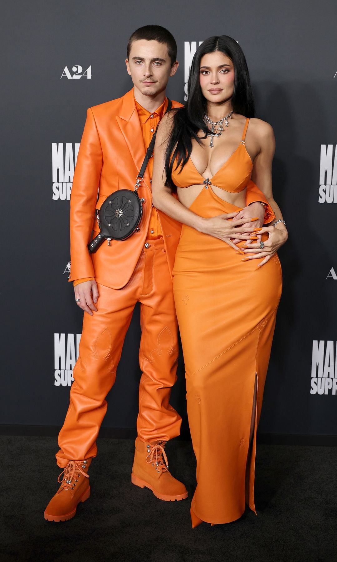 Pareja en la alfombra roja, él en traje naranja y ella en vestido naranja.