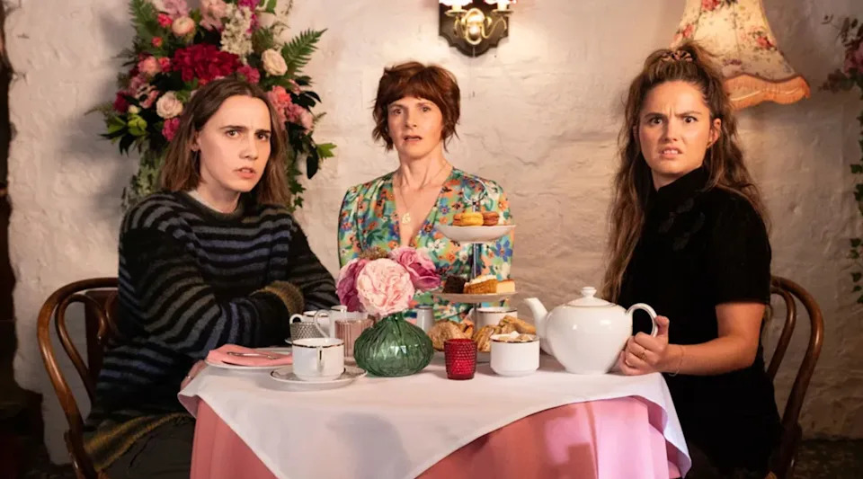 Tres mujeres sentadas a una mesa con tazas y galletas.