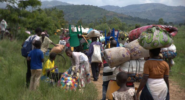 Un grupo de refugiados y solicitantes de asilo, incluidos niños, llevan sus pertenencias sobre la cabeza y la espalda mientras caminan por un campo de hierba en Burundi, huyendo de la violencia en el este de la República Democrática del Congo.