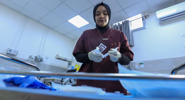 Una enfermera vestida con guantes de color marrón prepara suministros médicos en una habitación del hospital, centrándose en su tarea.