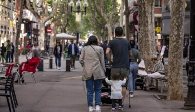 Una família, amb una nena petita, passeja per la rambla del Poblenou. De fons, més ciutadans circulant, alguns caminant i altres asseguts.