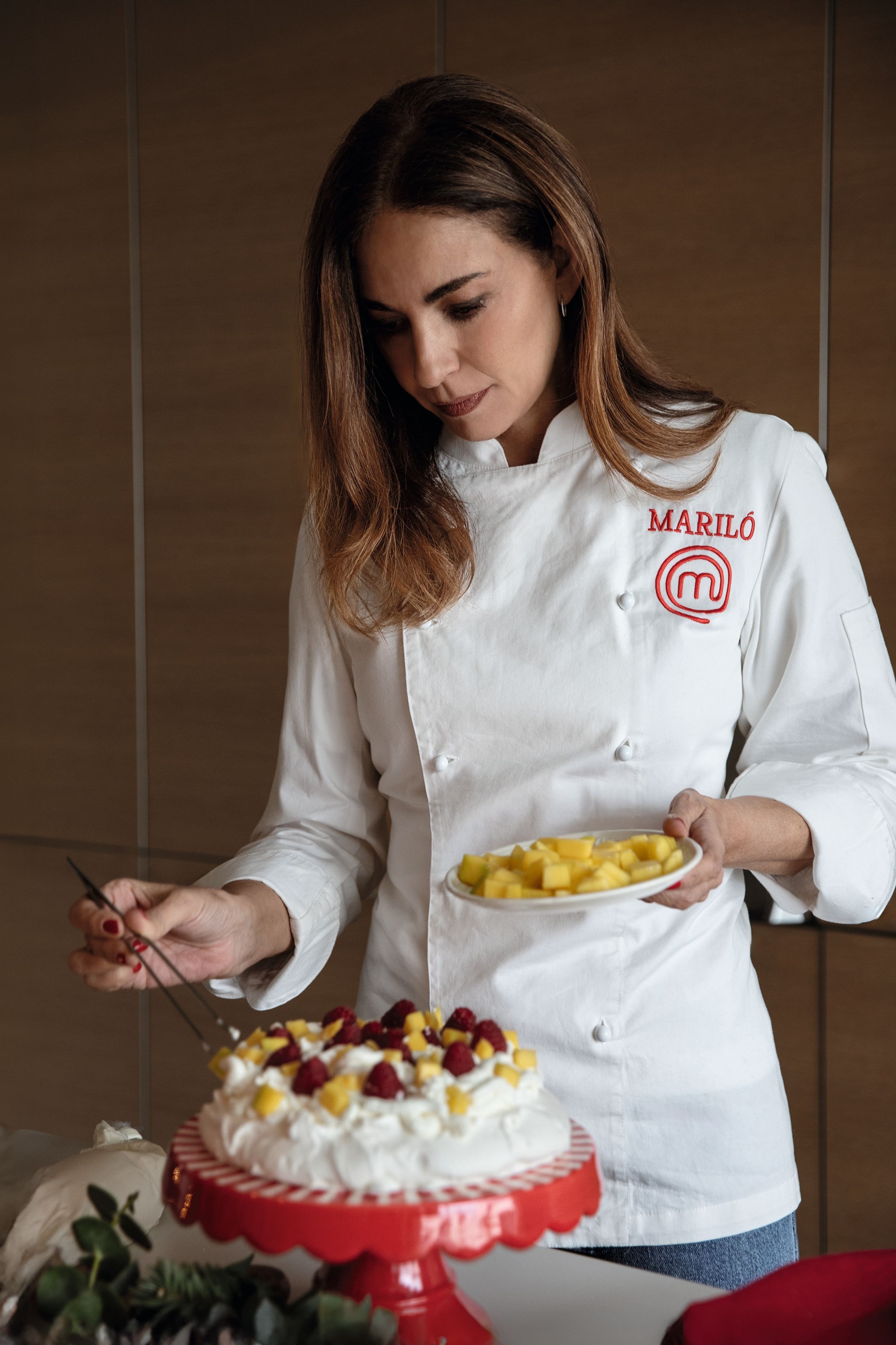 Mariló en uniforme de chef, sostiene un plato de pavlova con frutas.