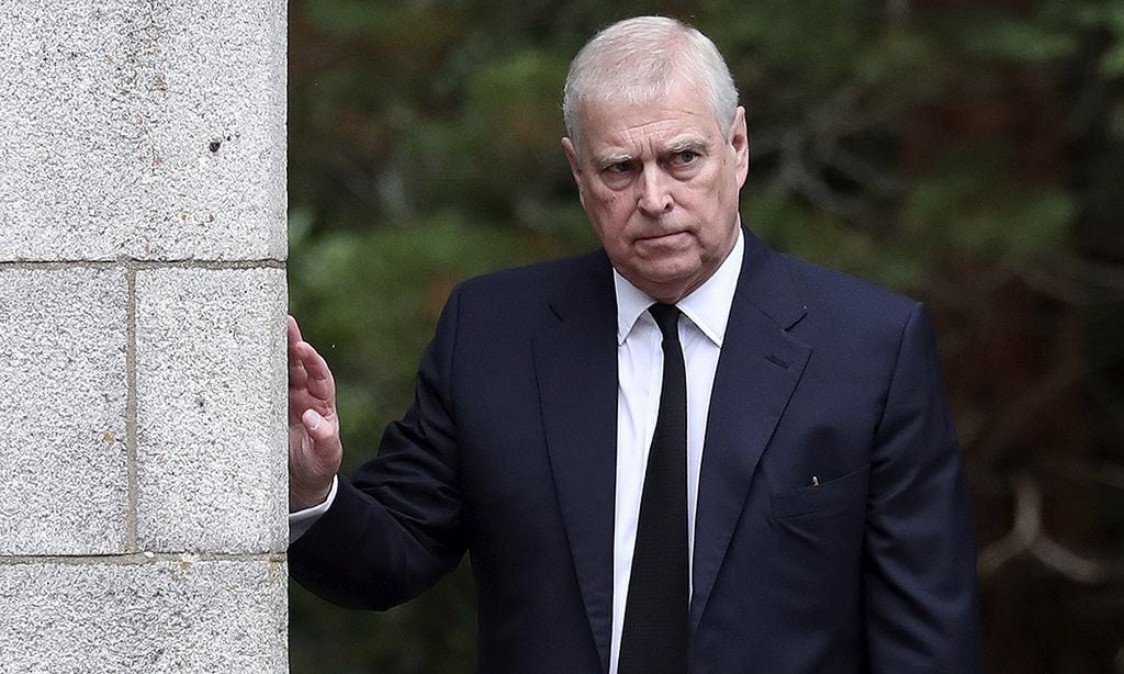 Príncipe Andrew, Duque de York, en traje azul, apoyado en una columna.