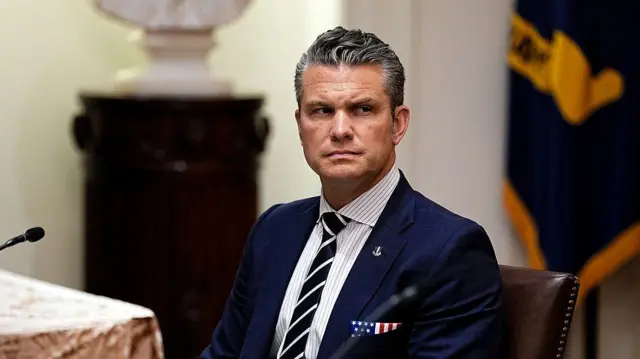 El secretario de Defensa, Pete Hegseth, sentado con una traje de corbata azul oscuro. El pañuelo en el bolsillo de su chaqueta tiene las barras y las estrellas de la bandera estadounidense. 