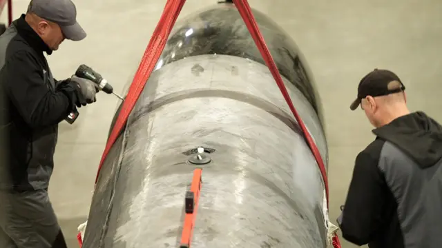 Dos hombres en vestimentas negras y gorros construyen un misil Flamingo en una fábrica secreta 