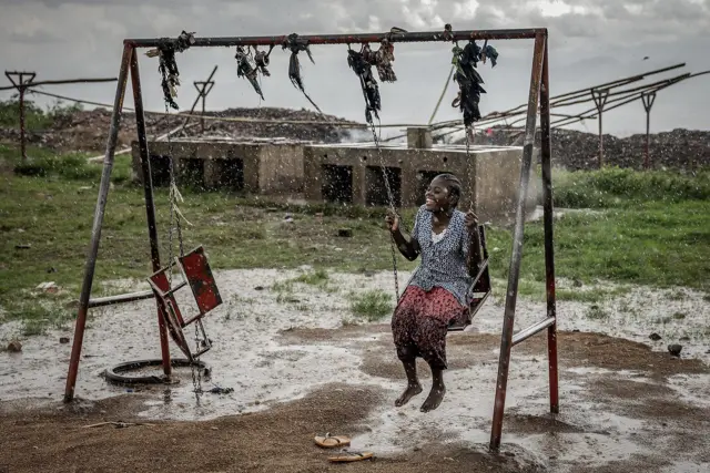Una mujer refugiada se balance en un columpio bajo la lluvia. 