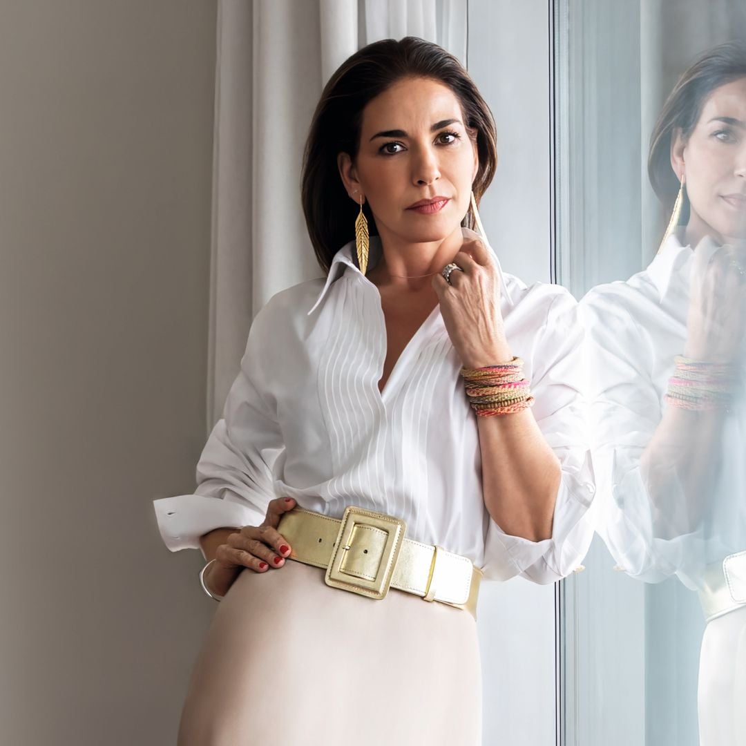 Mariló Montero  con cabello oscuro, camisa blanca y falda beige frente a un espejo.