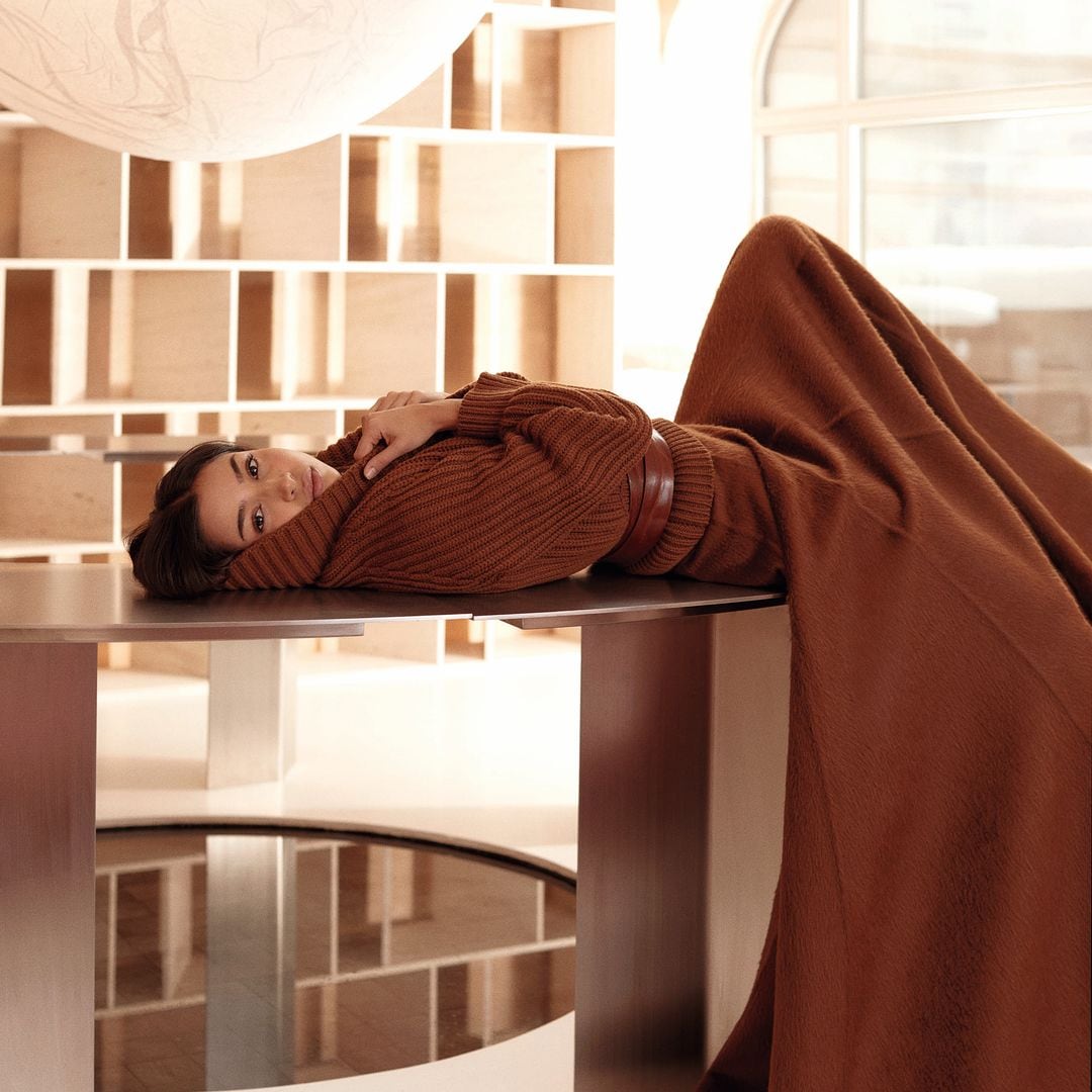 Najwa Khliwa sobre una mesa posa con un vestido marrón, una propuesta de Max Mara