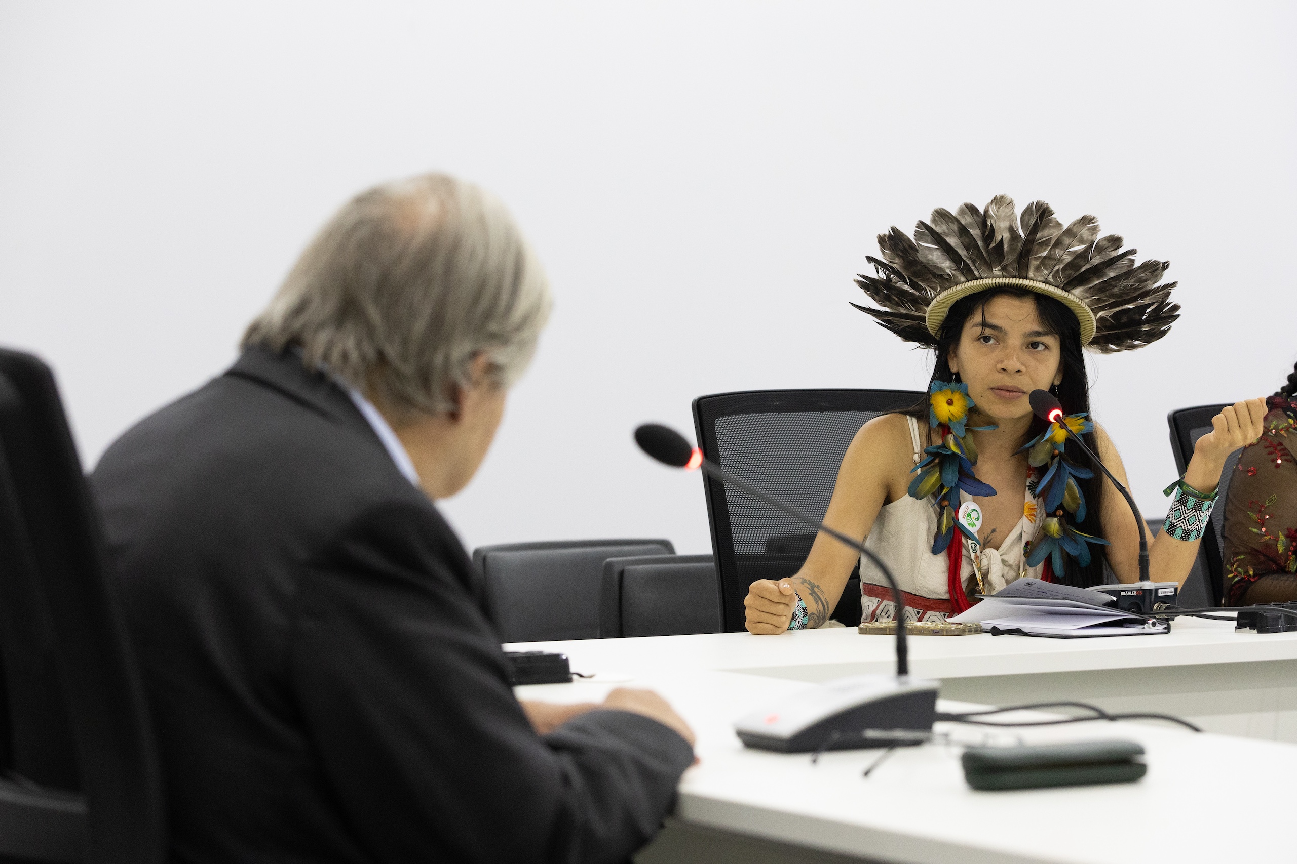 Una mujer con un tocado tradicional de plumas habla en una mesa de conferencias