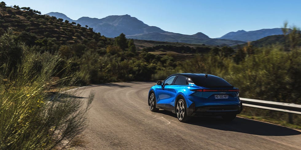 a blue car driving along a winding road with mountains in the background
