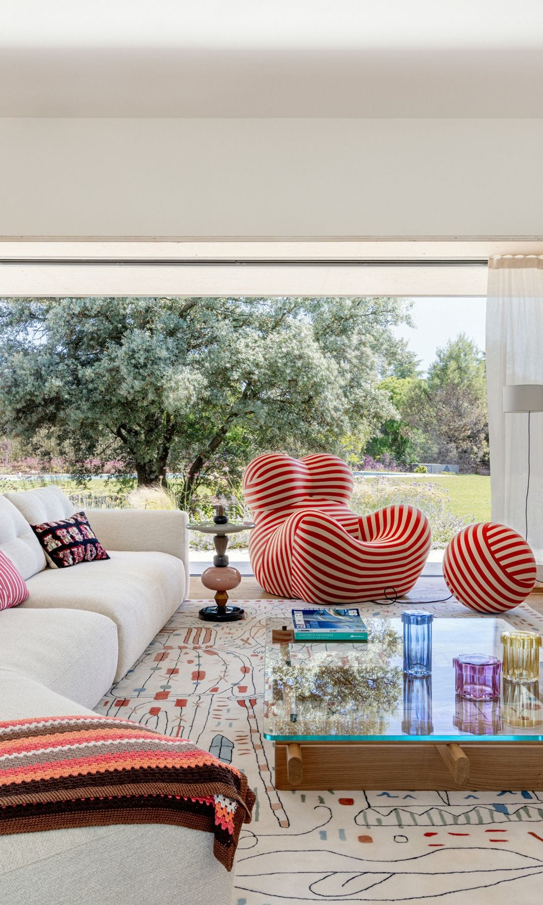 Salón abierto al exterior a través de un gran ventanal. La paleta cromática, cuidadosamente equilibrada entre tonos intensos y matices suaves, aporta frescura y contemporaneidad sin perder calidez