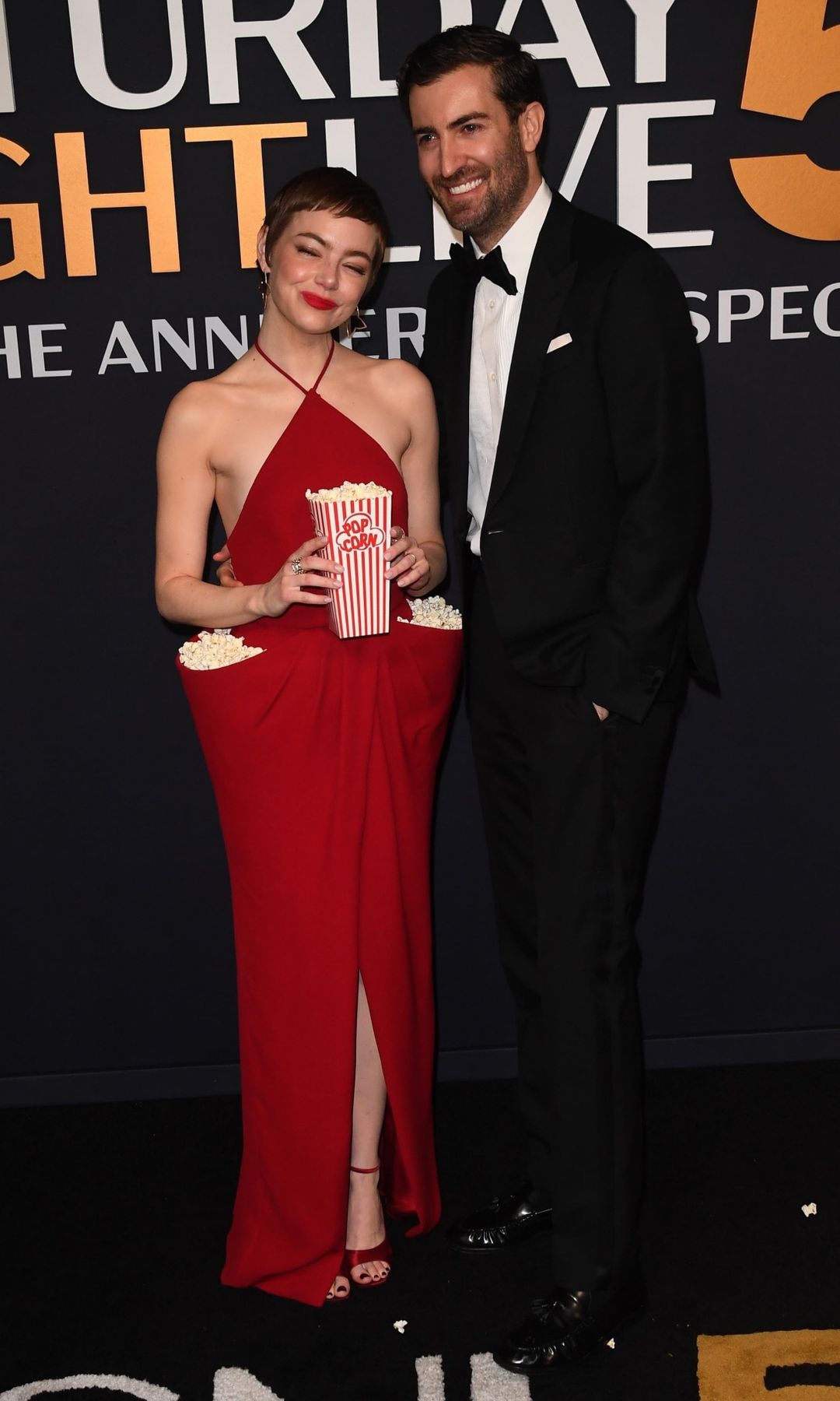 Emma Stone en un vestido rojo con palomitas de maíz, junto a un hombre en traje negro.