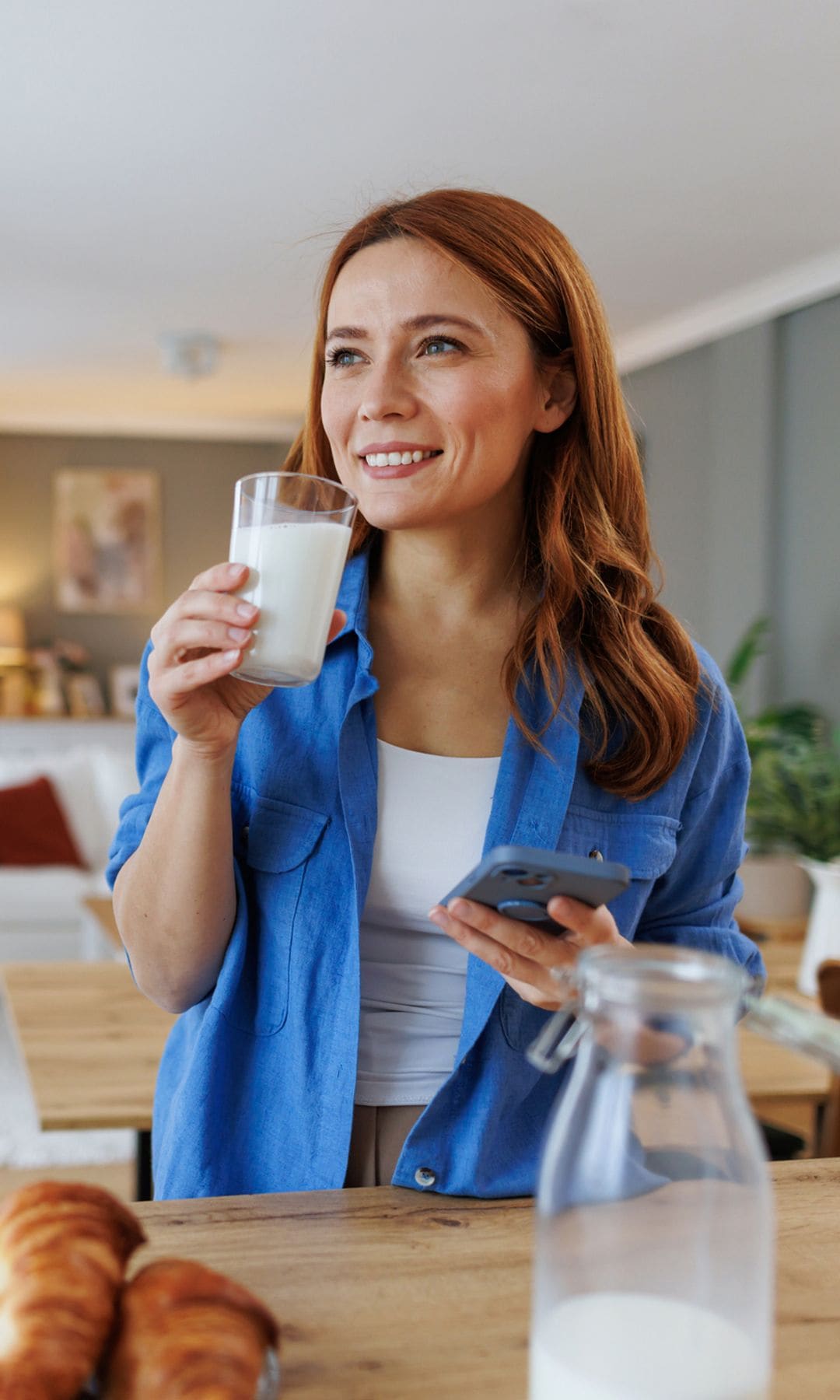 mujer bebiendo un vaso de leche en casa, con el móvil en la mano