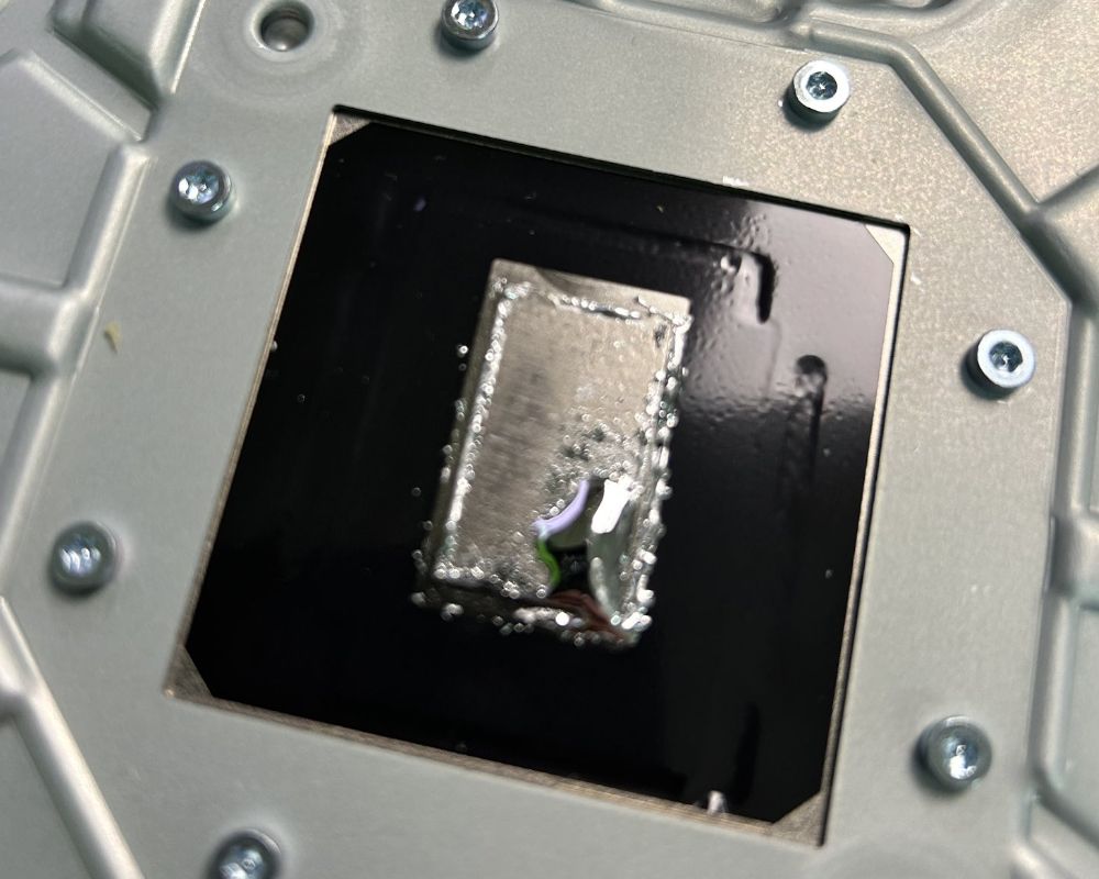 Detalle del procesador (APU) de una PS5 de un modelo anterior mostrando la aplicación del metal líquido sin barreras de contención perimetrales