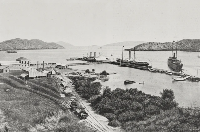 El puerto con unas pocas embarcaciones, líneas ferroviarias y casas pequeñas en medio de la vegetación