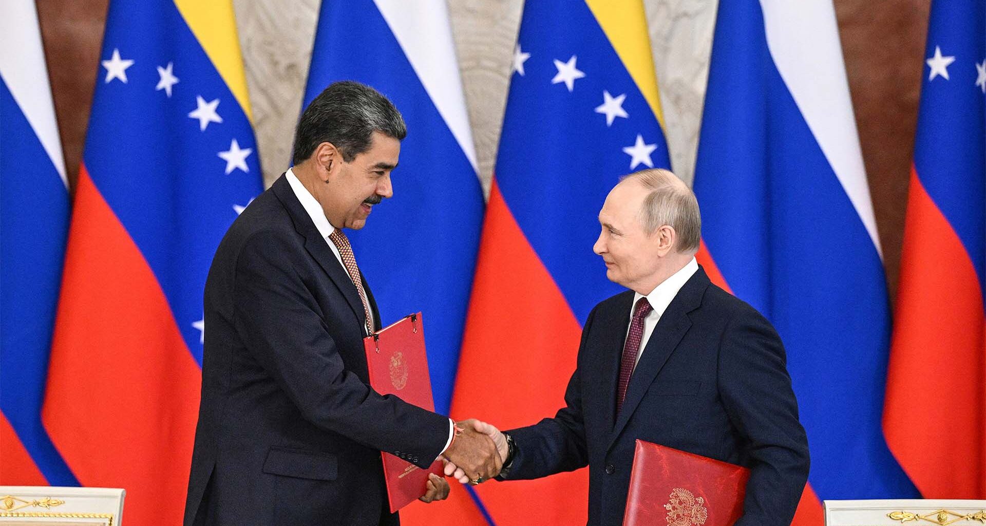 A la izquierda, Nicolás Maduro, expresidente de Venezuela, da la mano a Vladimir Putin, presidente de Rusia, en el Palacio del Kremlin, en Moscú (07/05/2025). Ambos portan una carpeta roja con el tratado de cooperación que acaban de firmar. Al fondo, varias banderas de Rusia y Venezuela.