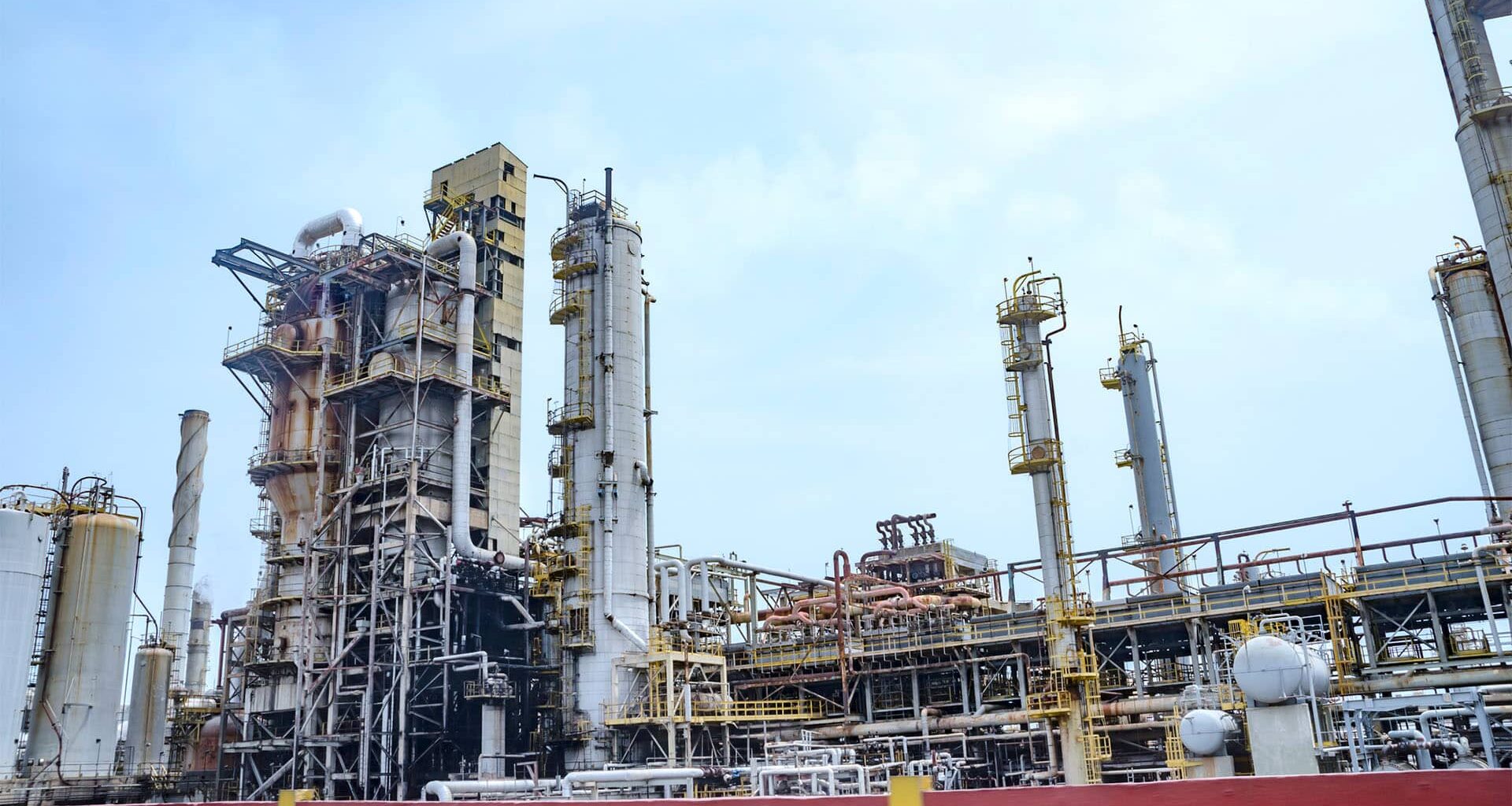 Planta de refinería de petróleo El Palito en Puerto Cabello (Estado Carabobo, Venezuela). En la imagen, múltiples torres de destilación de petróleo, hornos y una gran cantidad de sistemas de tuberías interconectados para su procesamiento. Al fondo, el cielo claro con algunas nubes.