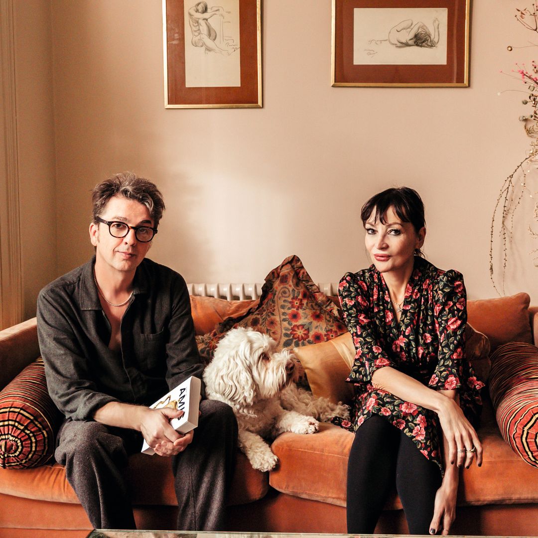 Danny Goffey y Pearl Lowe sentados en sofá con perro, en sala navideña.