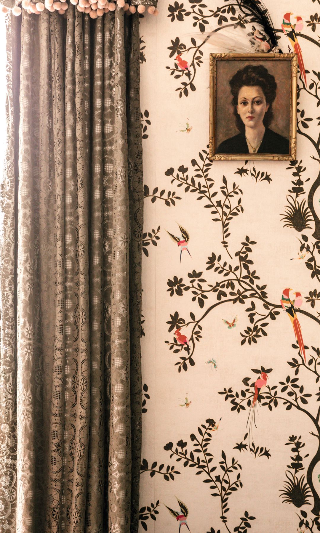 Cortina de encaje junto a una pared con mural de aves y un retrato de una mujer.