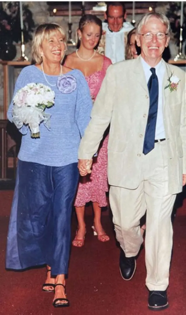 Daphne y Chuck saliendo de la iglesia el día de su boda en en el Valle de Napa. Daphne, quien sostiene un ramo de flores blancas, lleva una falda azul oscuro hasta los tobillos y un top de manga larga azul claro. Chuck, por su parte, lleva un traje de chaqueta beige, zapatos negros y una corbata azul oscuro a juego con la falda de Daphne.