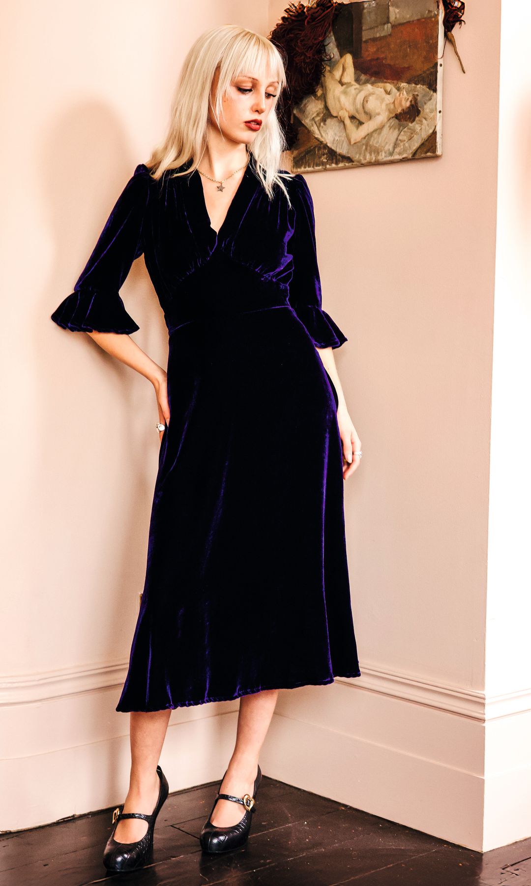 Mujer rubia con vestido azul oscuro y zapatos negros posa en un salón.