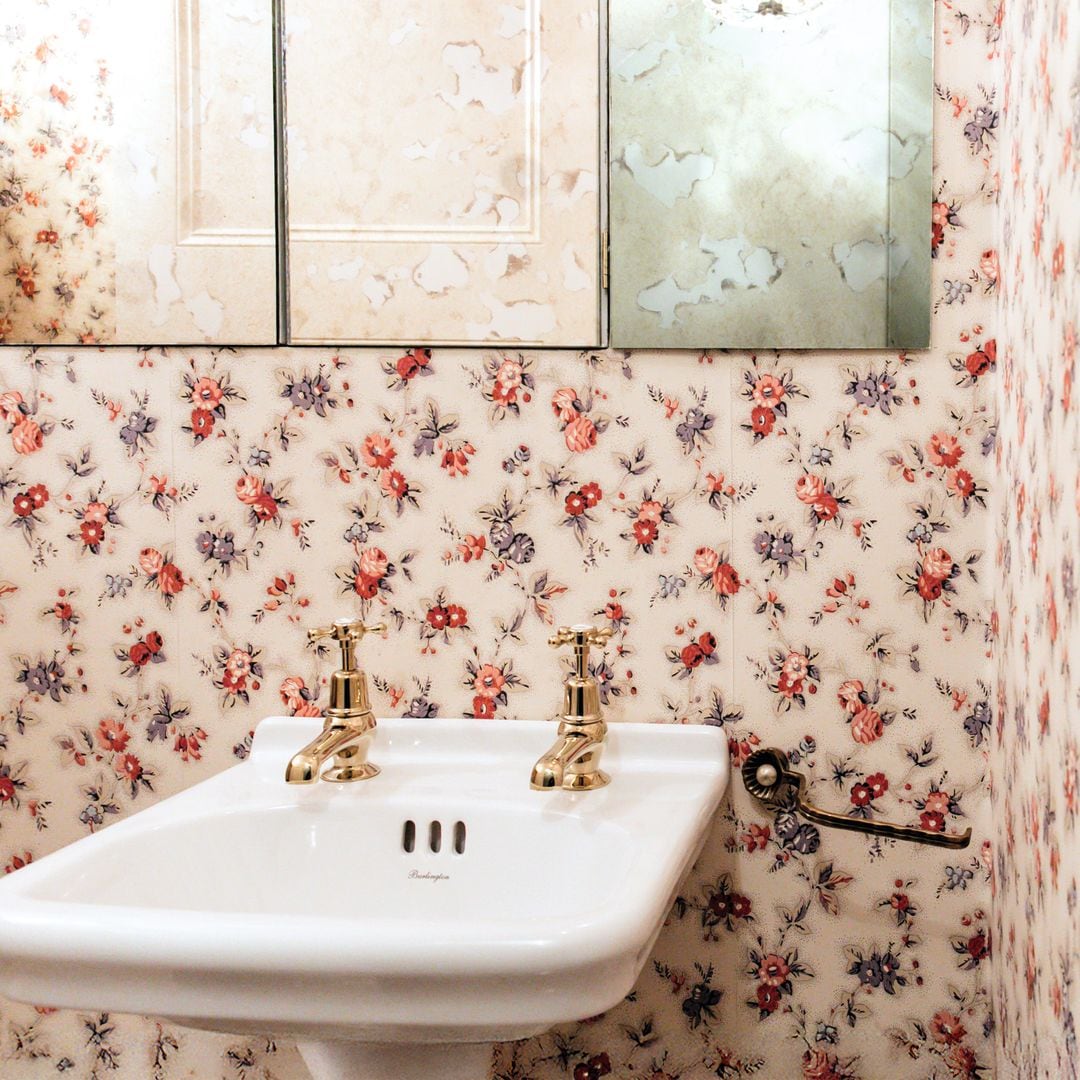 Baño con lavabo blanco, grifos dorados y papelera. No se detectan celebridades.
