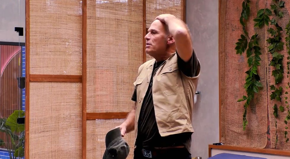 carlos lozano, con chaleco en color beige, se toca el pelo en la habitacion de la casa de gh duo