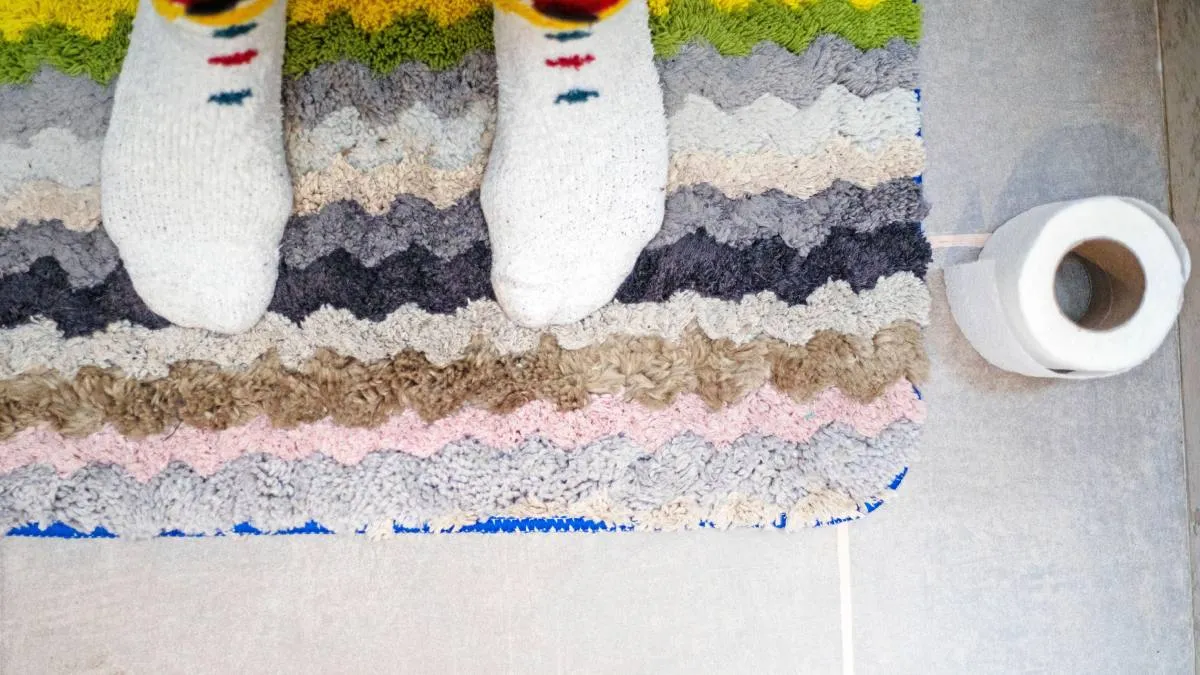 unos pies con calcetines sobre la alfombrilla de baño y un rollo de papel higiénico