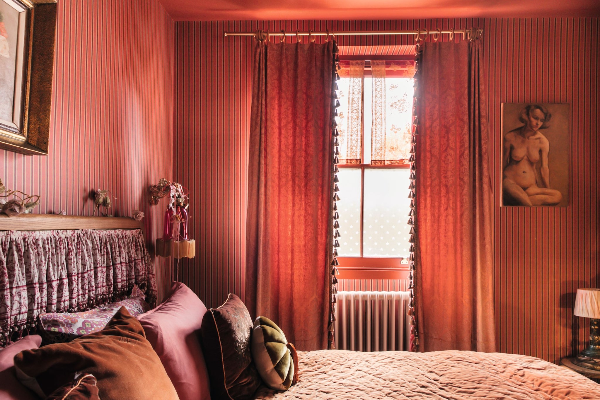 Habitación con cama, cortinas rojas, y cuadro de mujer desnuda