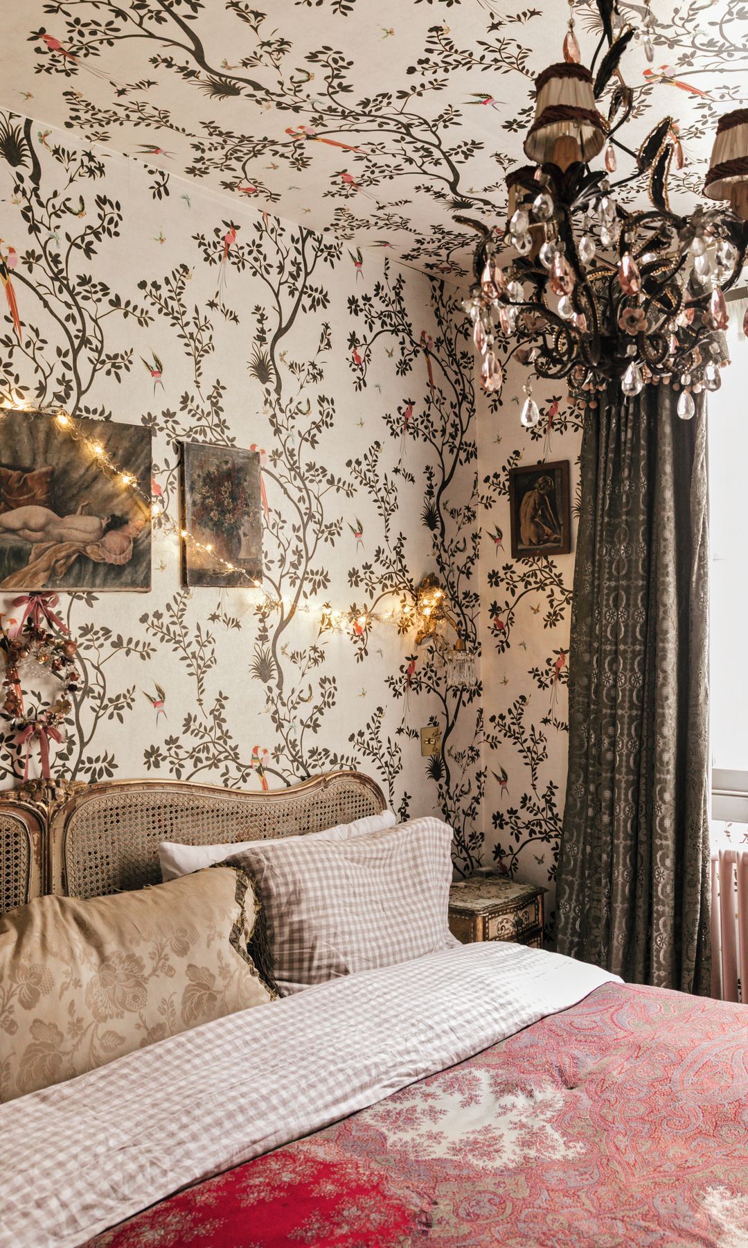 Habitación con cama, araña de cristal, cortinas y mural de árboles y pájaros.