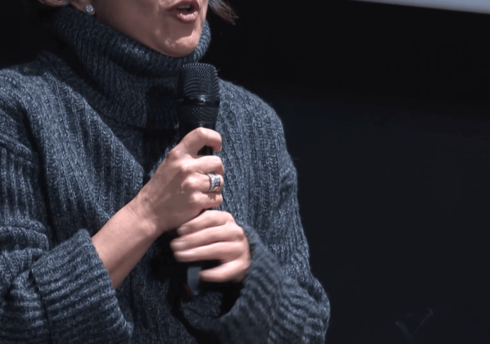 person speaking into a microphone while wearing a turtleneck sweater