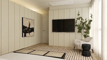 Un dormitorio luminoso con paredes paneladas claras, cama blanca, televisor, cuadro de mujer en caballo, sillón beige, mesa negra y planta verde junto a cortinas.