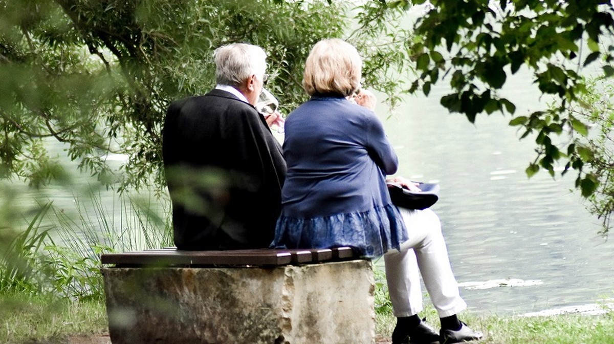 Bildbeschreibung: Eine ältere Frau und ein älterer Mann die auf einer Bank sitzen.