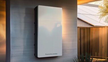A white energy storage unit mounted on a wall in a residential outdoor setting.