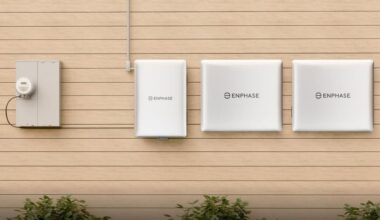 Enphase energy storage system with three white battery units and a meter on a wooden wall.