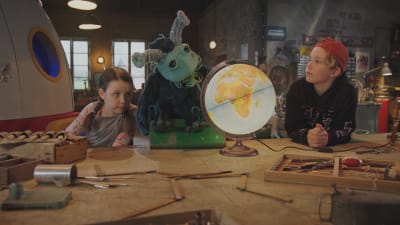 Kaksi lasta ja avaruusolionukke katsovat maapallolamppua.