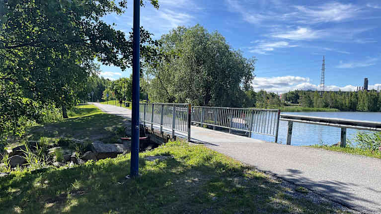 Kevyen liikenteen silta, oikealla vettä ja vasemmalla vehreää puustoa. 