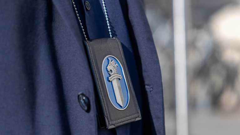 Poliisin virkamerkki roikkuu miehen kaulassa.