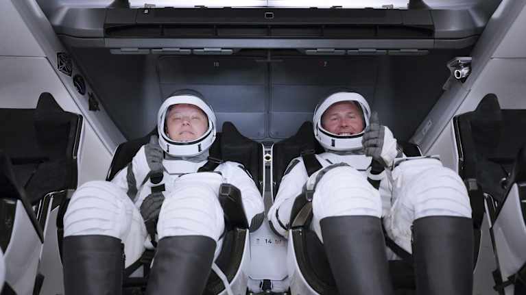 Kosmonautti Alexandr Gorbunov ja astronautti Nick Hague istuvat vierekkäin avaruuspuvut päällä raketin kyydissä ja näyttävät peukkua..