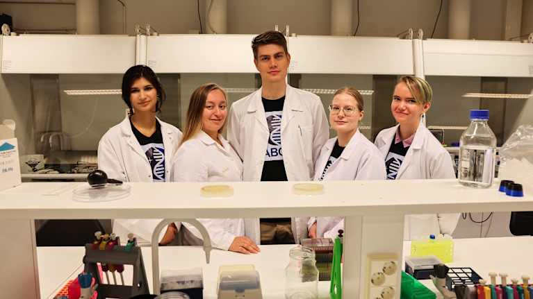 Viisi ihmistä seisoo laboratoriossa.